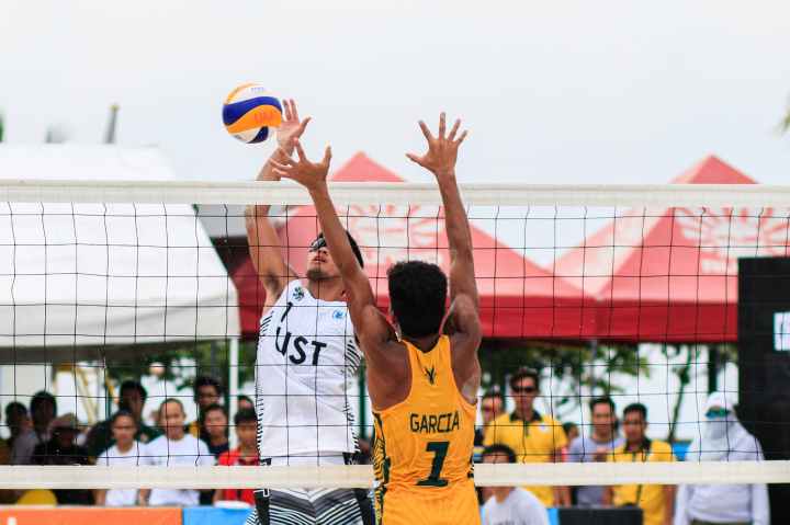 two men playing volleyball near red canopy